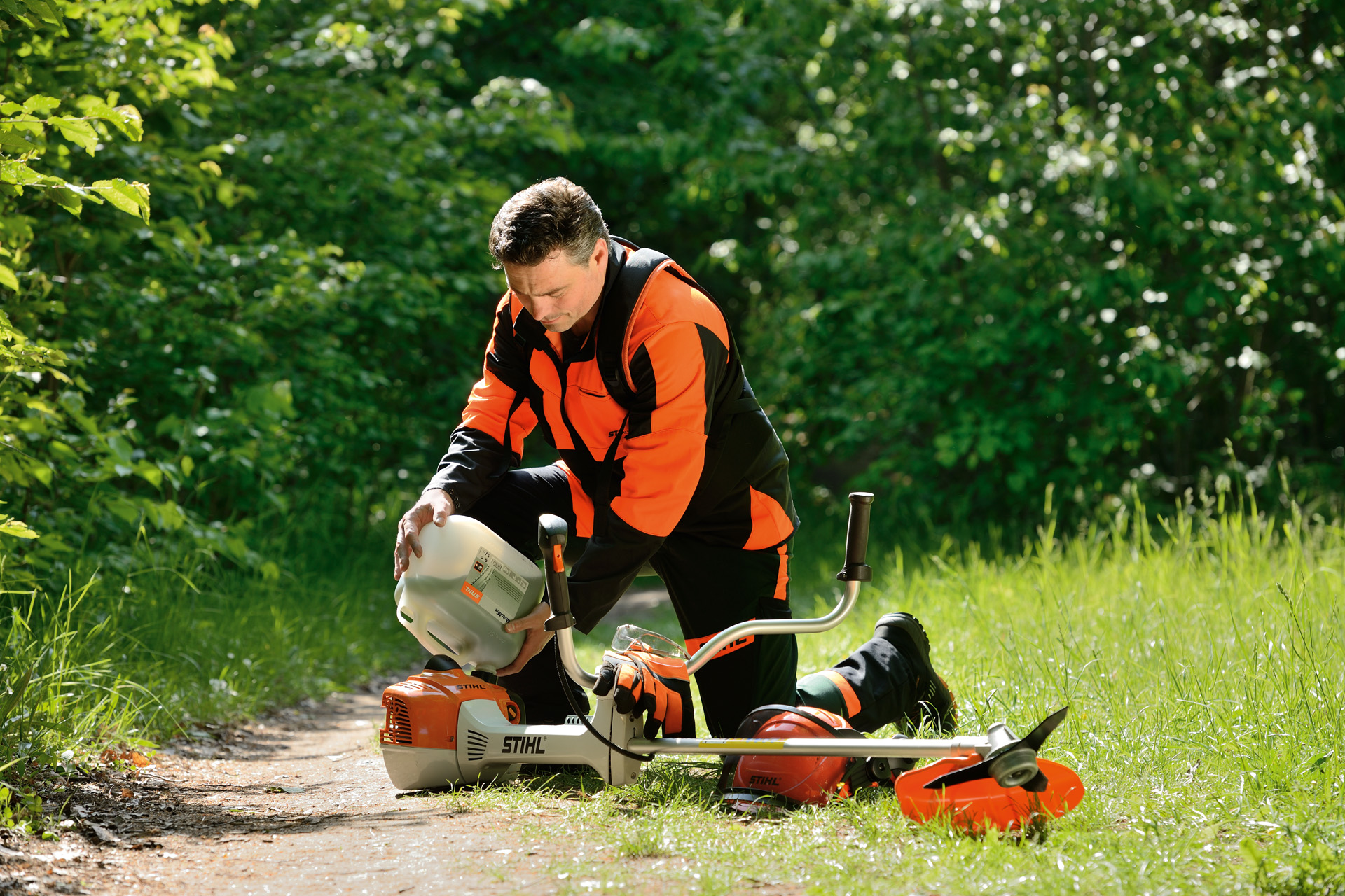 Un hombre llena el depósito de combustible de una motoguadaña STIHL con una garrafa con arbustos detrás de él