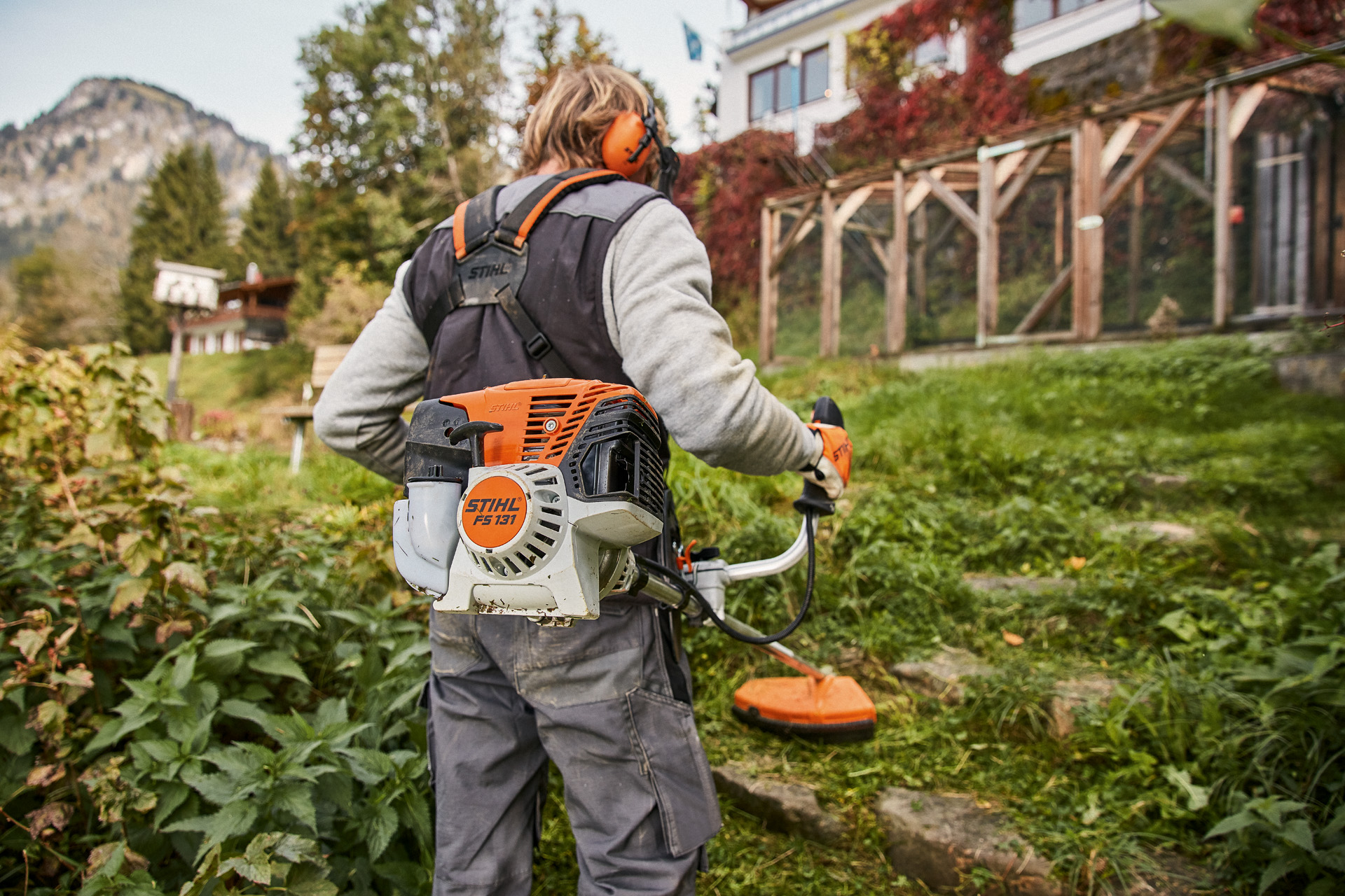 Un usuario con equipo de protección utiliza una motoguadaña a gasolina STIHL FS 131 en terrenos irregulares frente a una casa