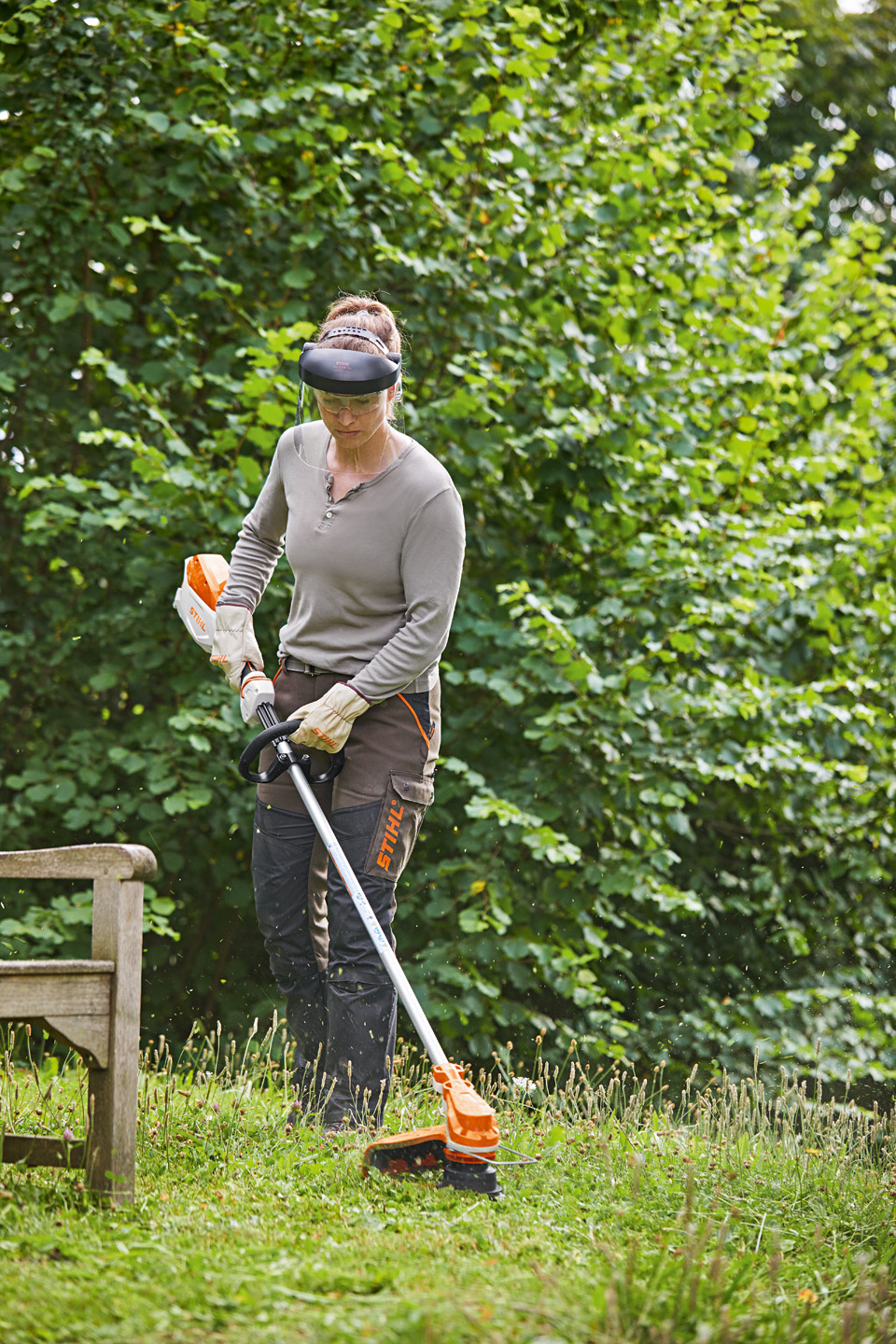 Una mujer corta la hierba alrededor de un pequeño árbol con una guadaña a batería STIHL AK FSA 60 R